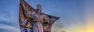 Statue of a native american person holding a diamond quilt over their shoulders