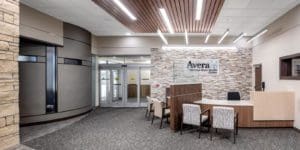 Interior of a medical facility with a brick wall backsplash and a wooden reception area with white chairs.