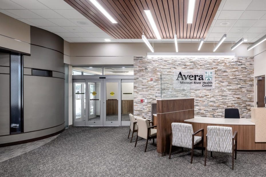 Interior of a medical facility with a brick wall backsplash and a wooden reception area with white chairs.