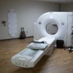 Cat scan machine in a medical office with hardwood floors and white walls with brown wooden cabinets.