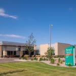 exterior of a medical facility with tan siding and green yard with black parking lot.