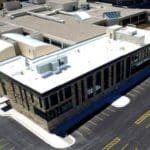 Birds eye view of a brick building with a white roof and black parking lot.