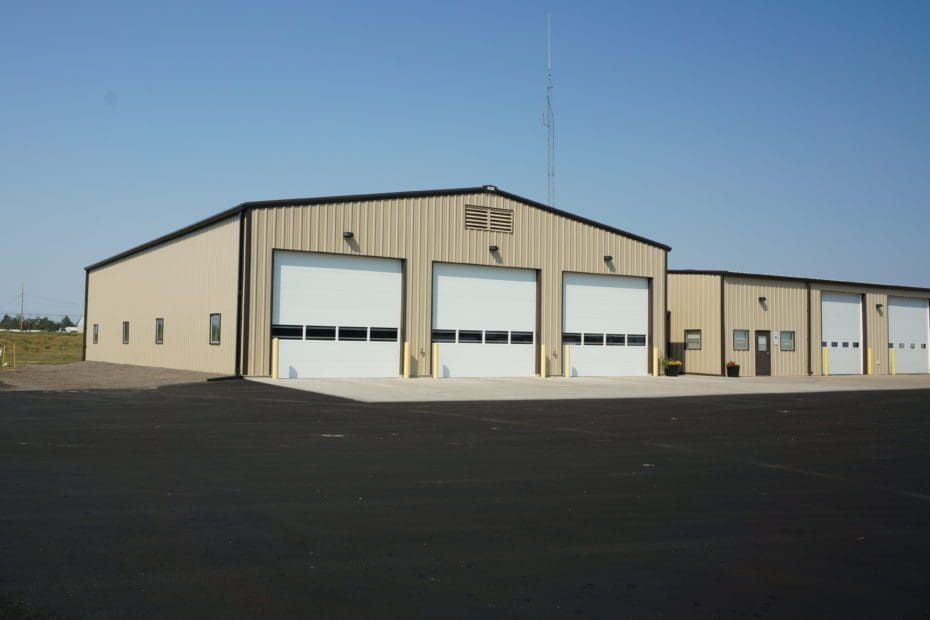 Exterior of a warehouse garage with white doors and tsn siding, and a blacktop in front.