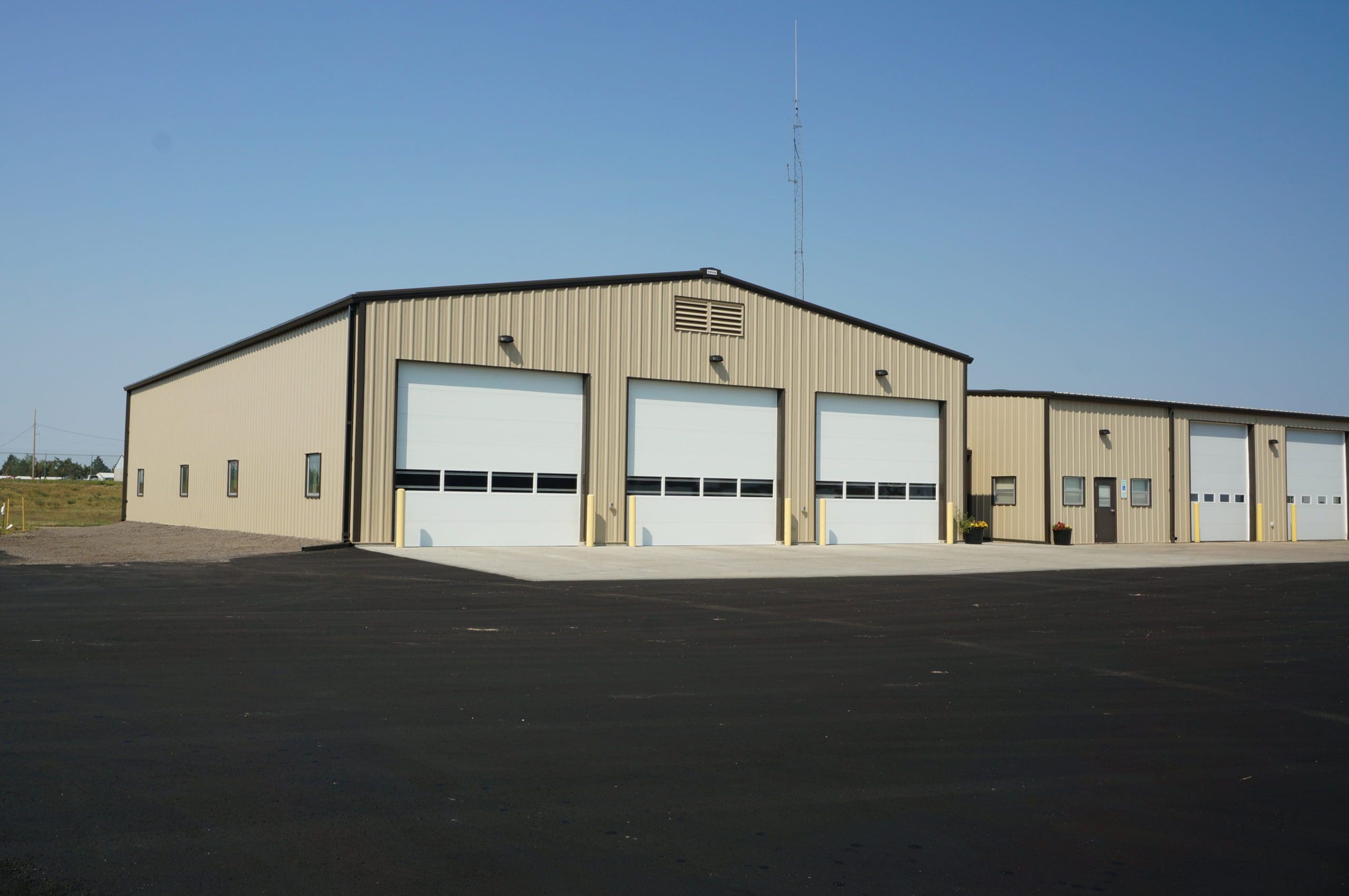 Exterior of a warehouse garage with white doors and tsn siding, and a blacktop in front.